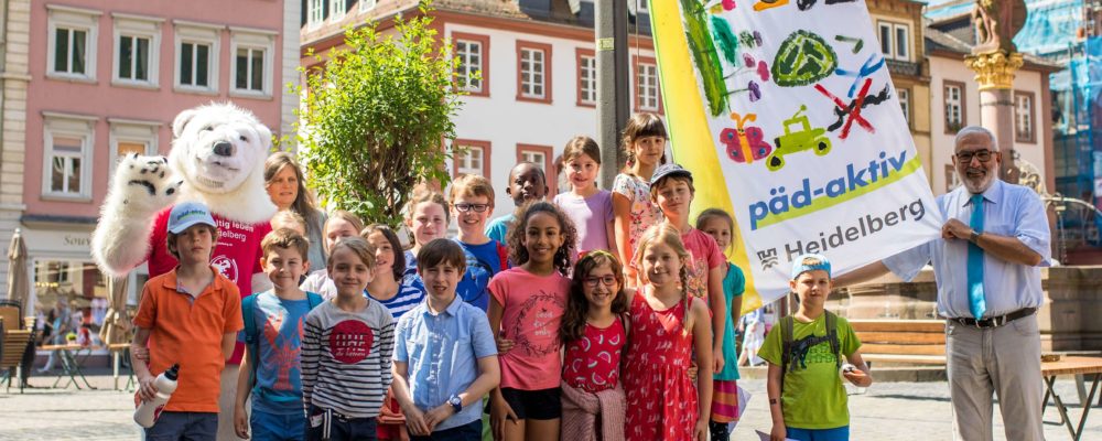 Abschlussfoto des zweiten Heidelberger Kinderklimagipfels: Gemeinsam mit Bürgermeister Wolfgang Erichson (re.) und Umweltamtsleiterin Sabine Lachenicht (hintere Reihe neben dem Eisbär-Maskottchen) hissten die Kinder vor dem Rathaus ihre selbstgestaltete Klimaschutz-Flagge. (Foto: Dittmer)